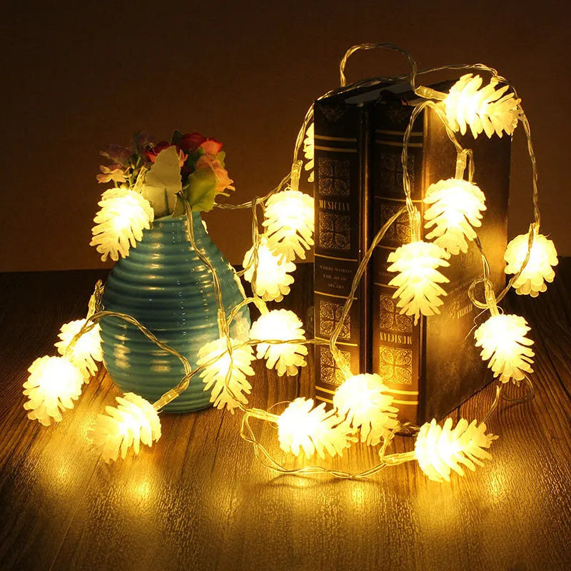 Warm white LED pine cone decorative light string powered by batteries on a green foliage background.