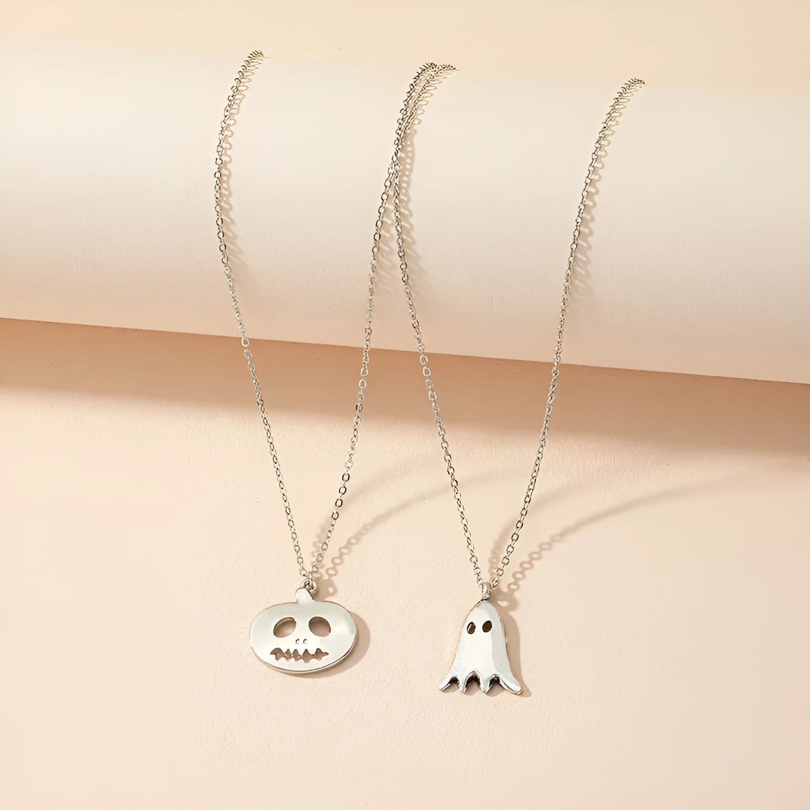 Two silver alloy pendant necklaces: one cartoon pumpkin and one cartoon ghost on a light background