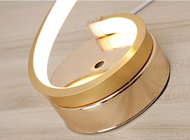 Modern LED table lamp with gold metal base and curved acrylic shade on a desk