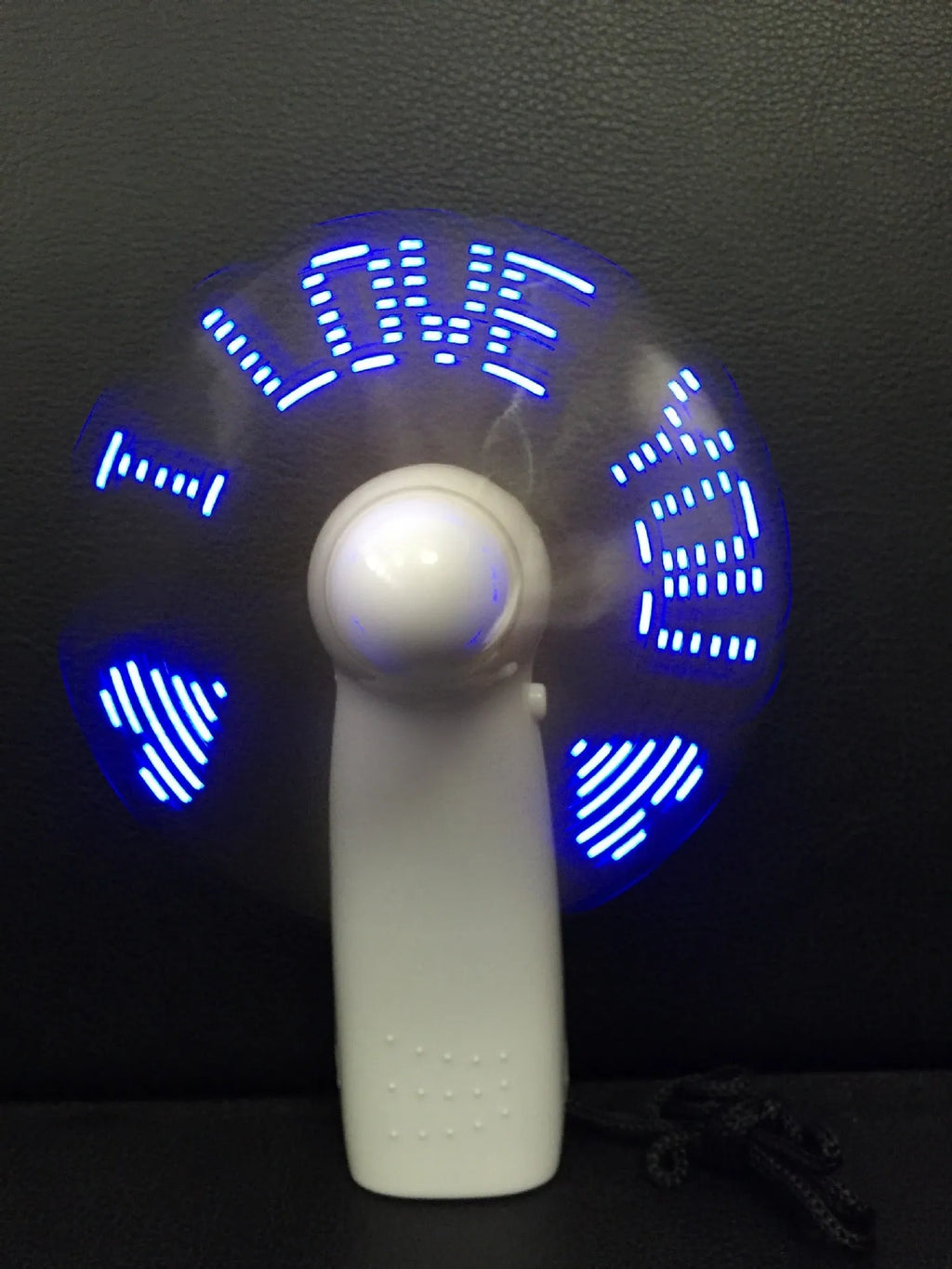 White handheld mini fan with LED lights displaying a love heart pattern, shown next to AAA batteries for scale.