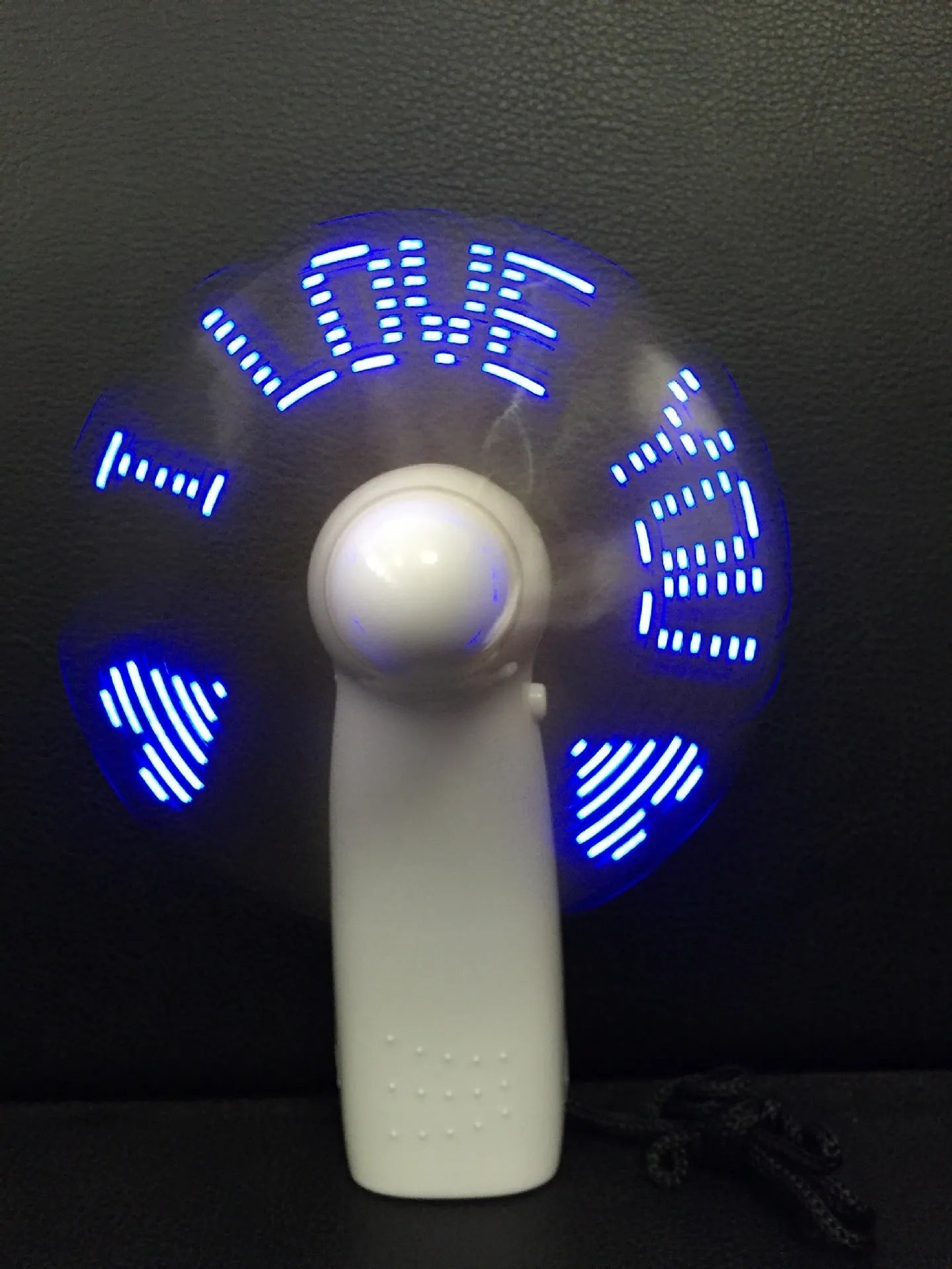 White handheld mini fan with LED lights displaying a love heart pattern, shown next to AAA batteries for scale.