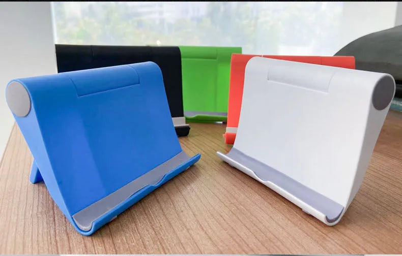 Black PE folding tablet stand holding a mobile phone at an adjustable viewing angle on a wooden desk.
