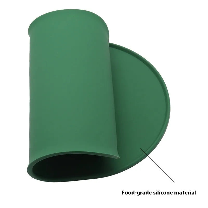 Green silicone cat feeding mat with raised edge under a ceramic bowl on a wooden floor