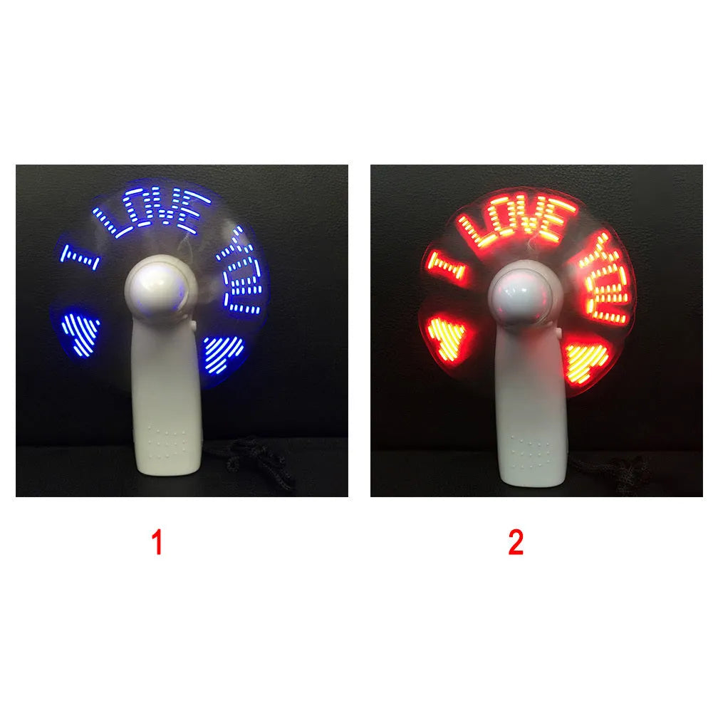 White handheld mini fan with LED lights displaying a love heart pattern, shown next to AAA batteries for scale.