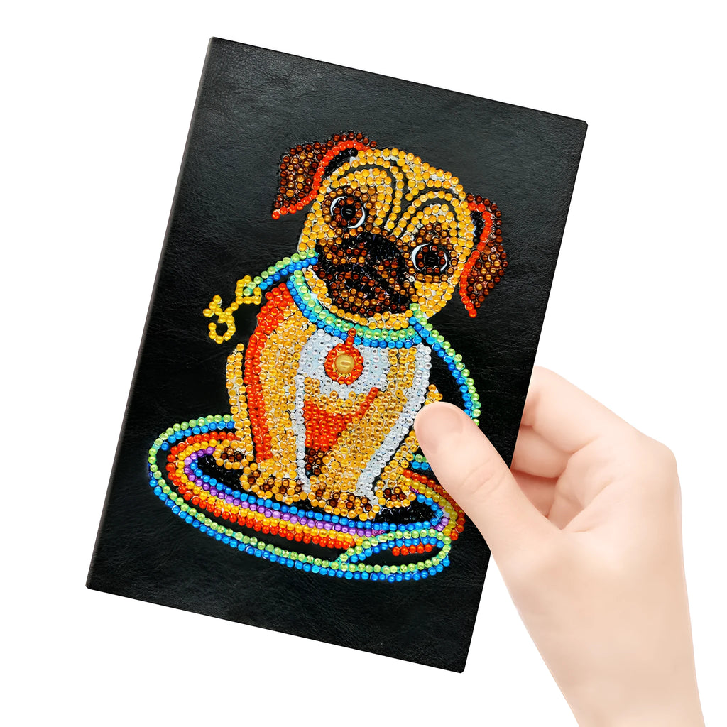 Black A5 hardcover diamond painting notebook with elastic closure, shown closed and open on a crafting table.