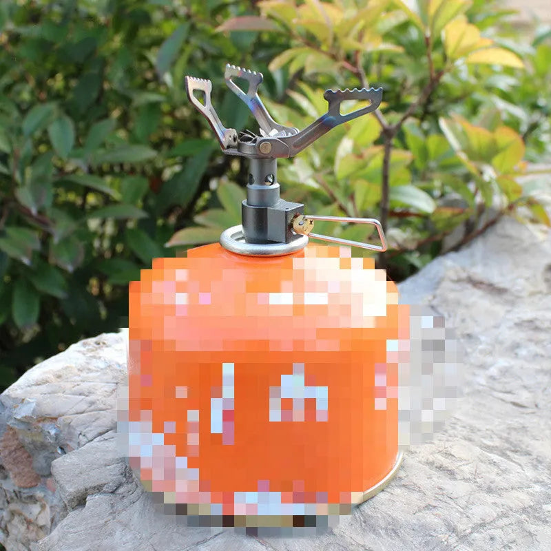 Compact one-piece propane camping stove on rocky ground, fuel canister attached, with a pot boiling.