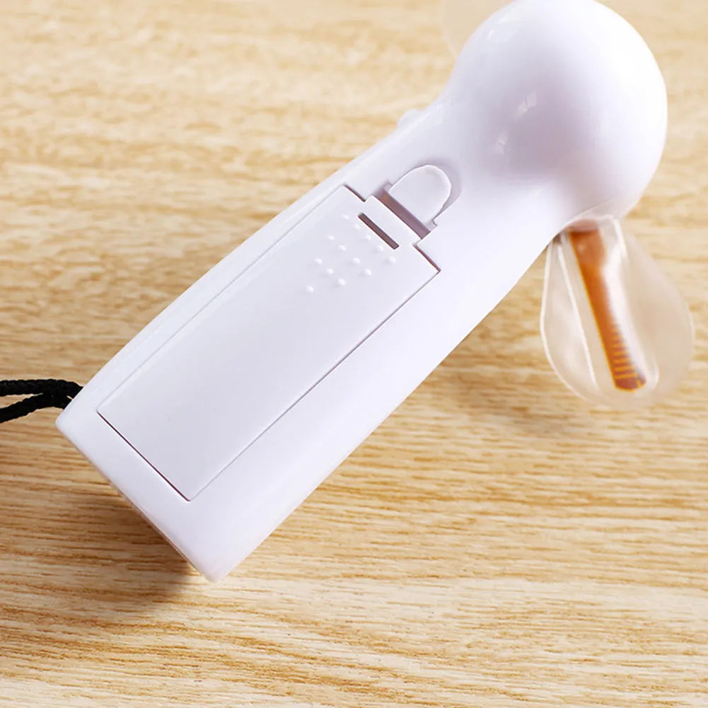 White handheld mini fan with LED lights displaying a love heart pattern, shown next to AAA batteries for scale.