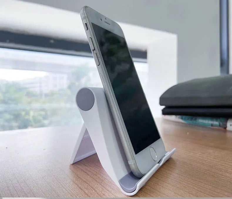 Black PE folding tablet stand holding a mobile phone at an adjustable viewing angle on a wooden desk.