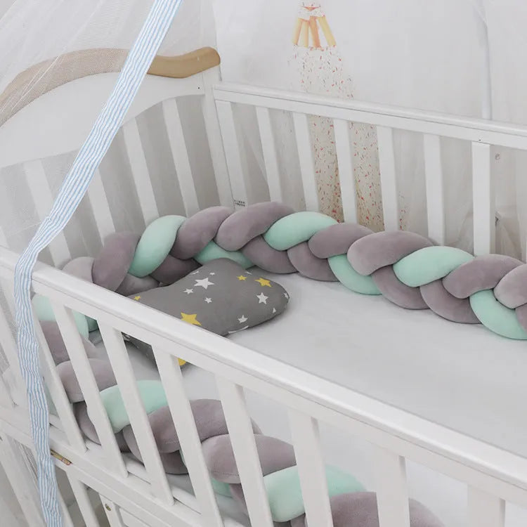 Close-up of a grey braid knot pillow cushion cot bumper fitted around white crib rails.