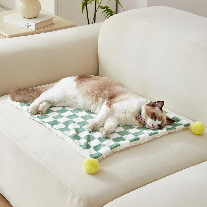 Green plaid pattern fleece pet blanket with a fur ball decoration, shown on a sofa.