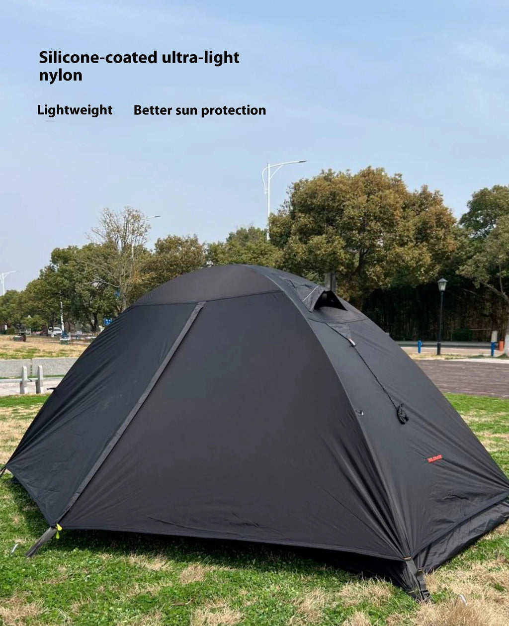 Red single-person double-layer backpacking tent with aluminium poles pitched in a grassy field