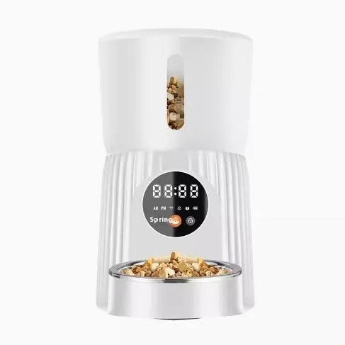 Black automatic pet feeder with digital timer display and remote control on a table.