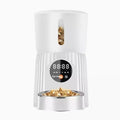 Black automatic pet feeder with digital timer display and remote control on a table.