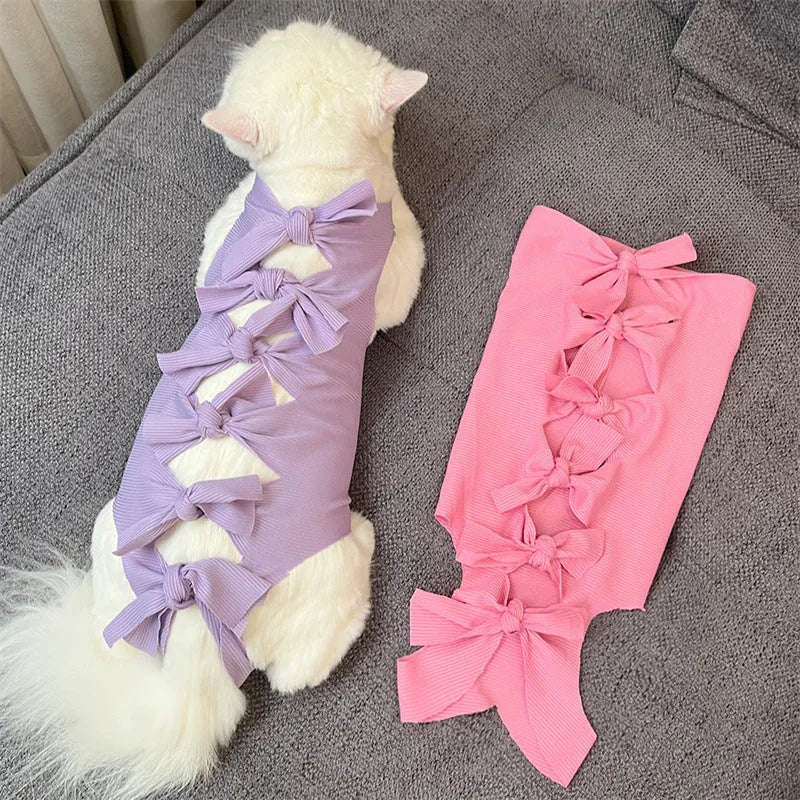 Pink lace-up cat recovery bodysuit on a table, showing back ties and full-body design for post-surgery care.