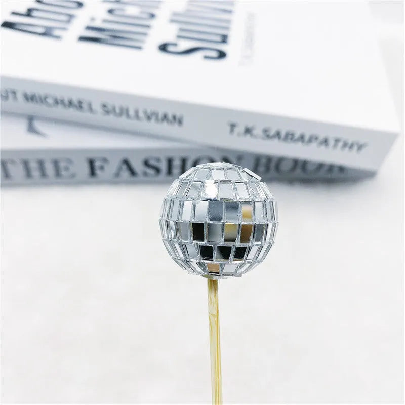 Small glass mirrored disco ball cake decoration attached to a thin wooden stick.