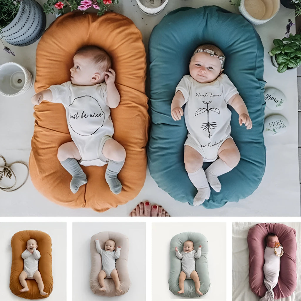Beige portable baby nest cot crib for infants on a neutral background
