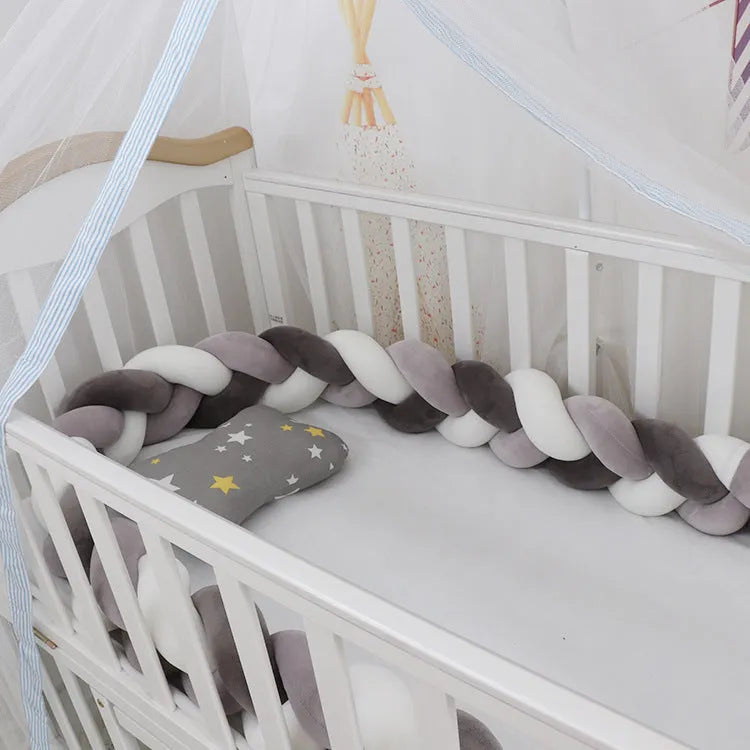 Close-up of a grey braid knot pillow cushion cot bumper fitted around white crib rails.