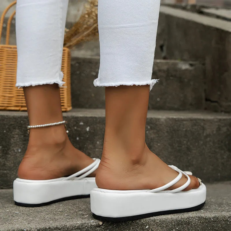 A pair of thick-soled herringbone pattern flip-flop slippers on a solid background.