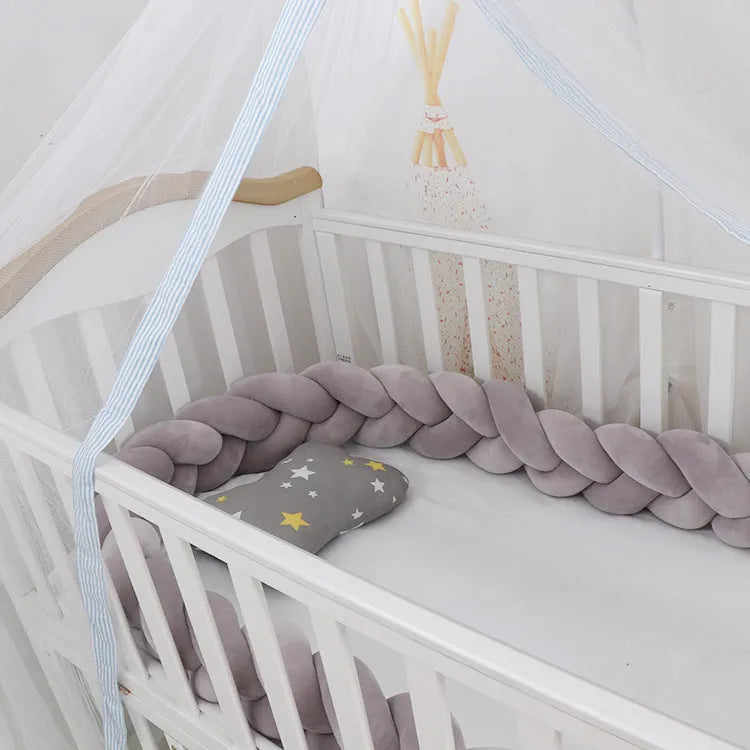 Close-up of a grey braid knot pillow cushion cot bumper fitted around white crib rails.