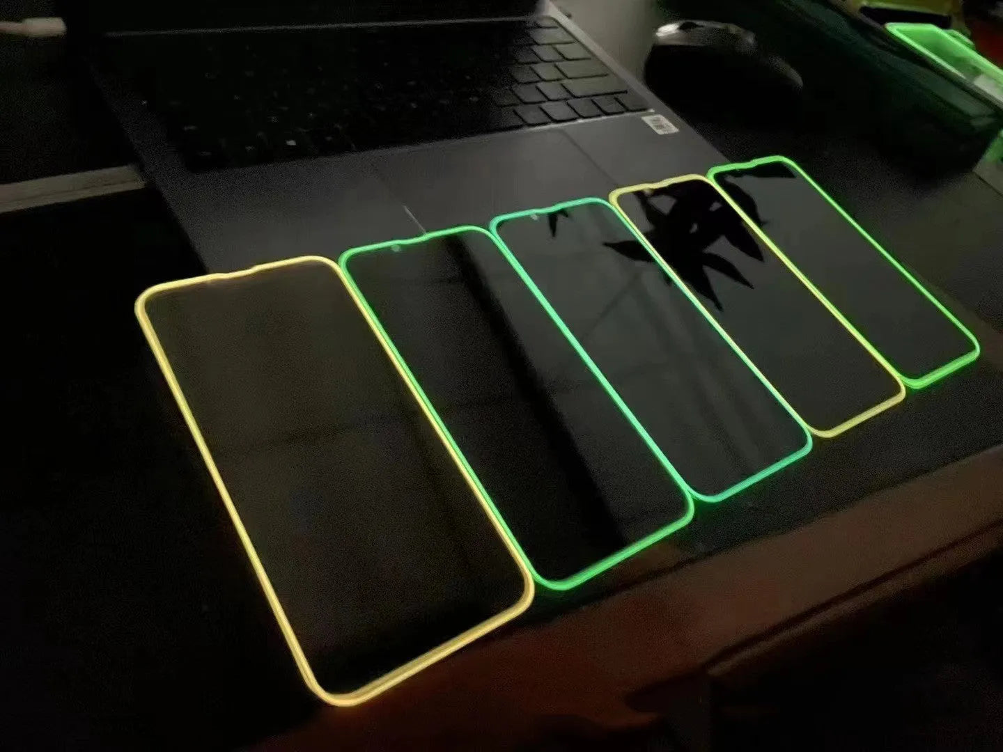 Fluorescent pink tempered glass screen protector glowing on an iPhone 13 in a dark room.