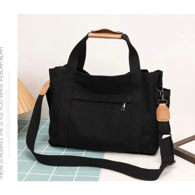 A horizontal square canvas tote bag in army green with a cross-body strap and visible sewing lines.