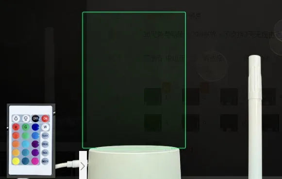 Black 3D acrylic message board night light with remote control and stylus on desk.