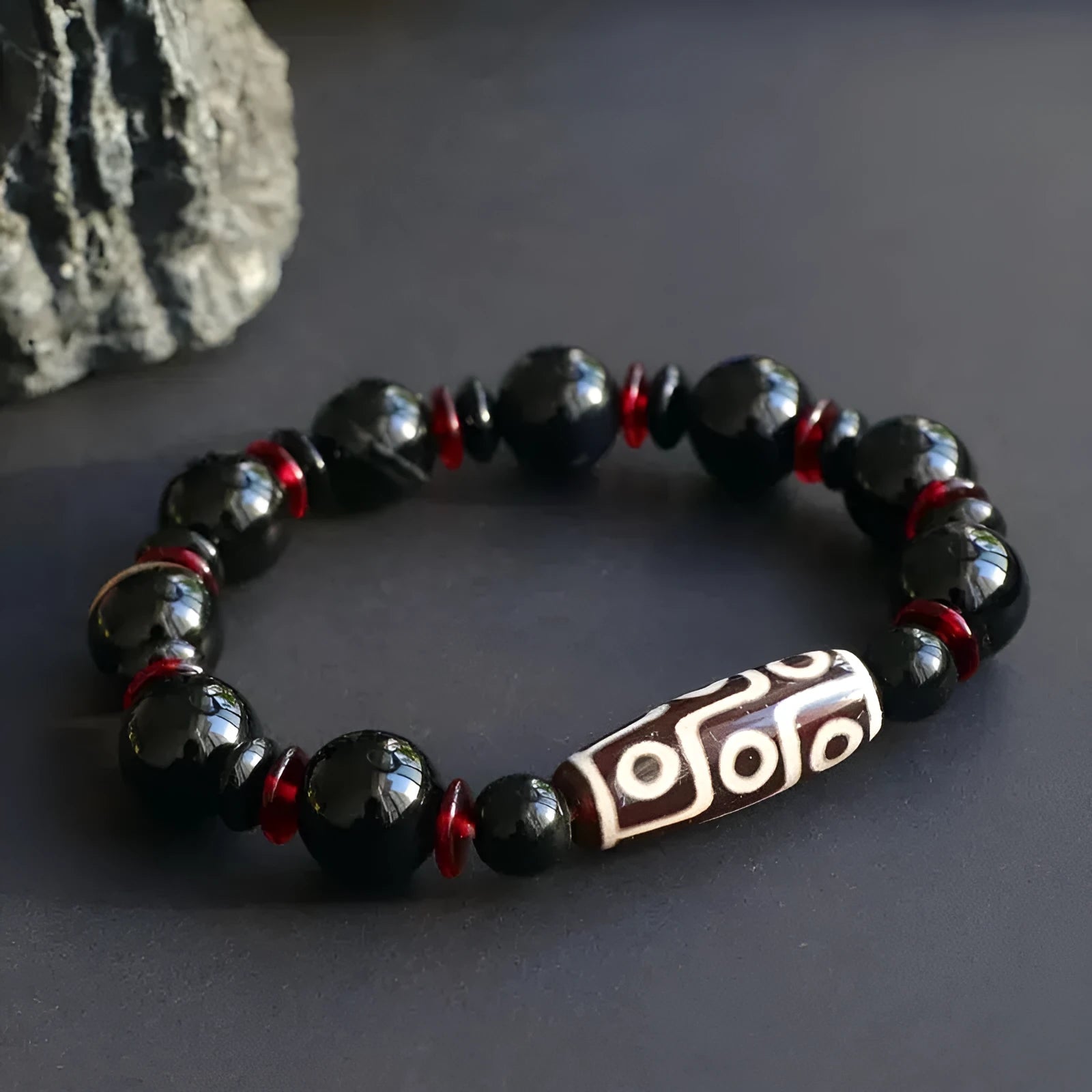 Hand-woven black agate dzi bead bracelet with geometric chalcedony beads on a wrist.