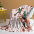 Pink hummingbird floral fleece throw blanket made of soft flannel velvet, folded on a sofa