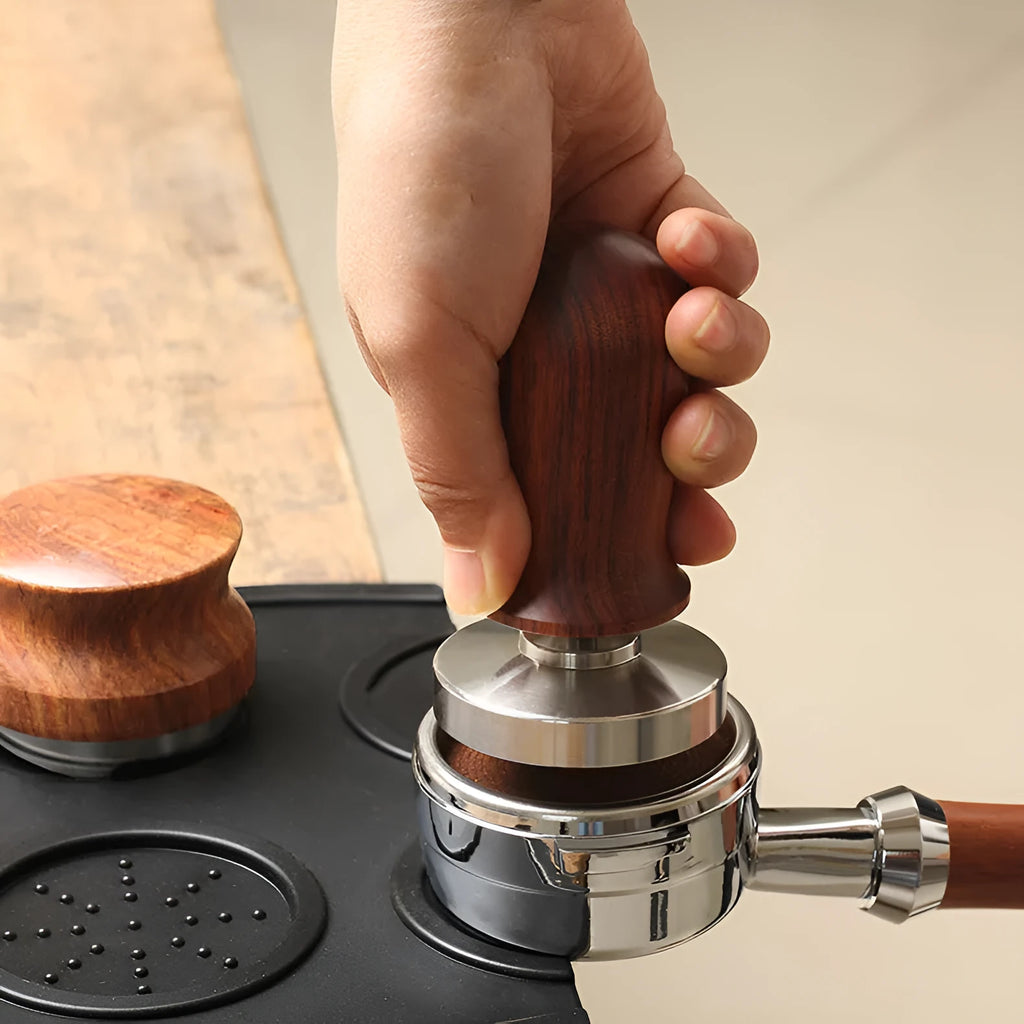 Black and red coffee tamper powder press tool with stainless steel base on a wooden table.