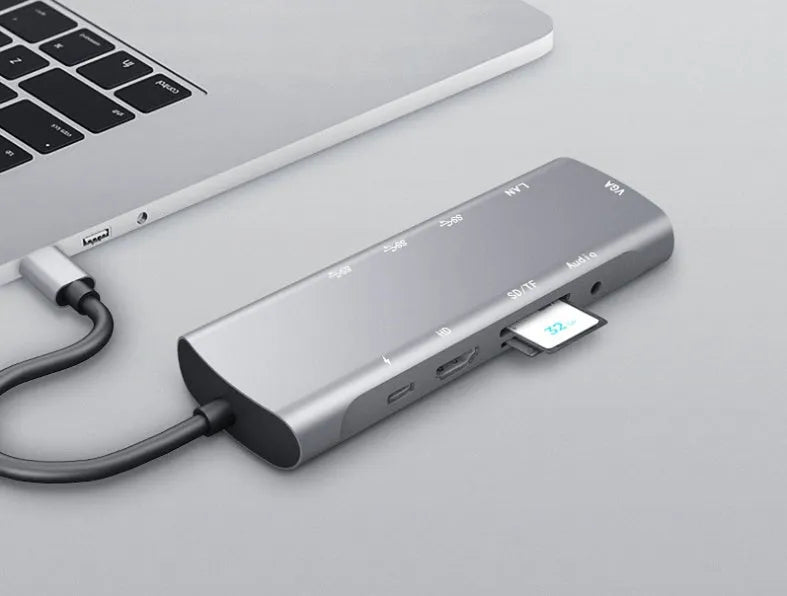 Grey aluminium USB-C docking station with HDMI, VGA, USB 3.0, and PD charge ports on a desk.
