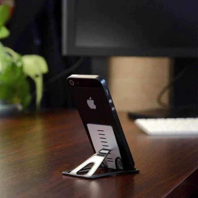 Black desktop card phone holder on a wooden desk next to a mobile phone and credit cards