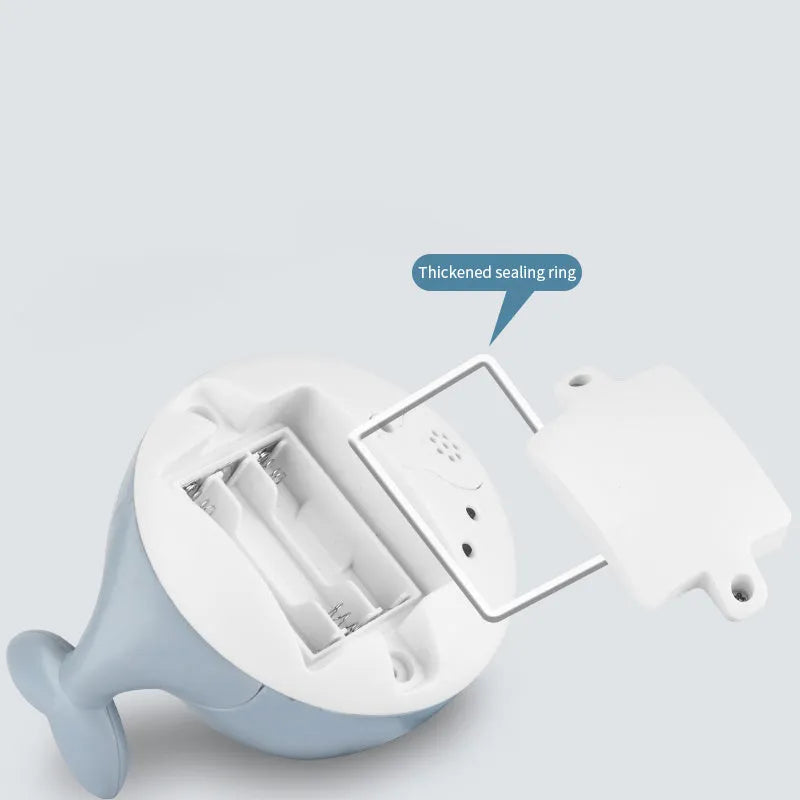 White and blue whale bath toy spraying water with LED lights on, floating in a bathtub