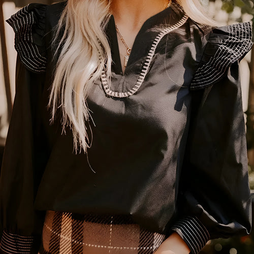 Black women's V-neck blouse with ruffle detailing on the long sleeves and contrast stitching.