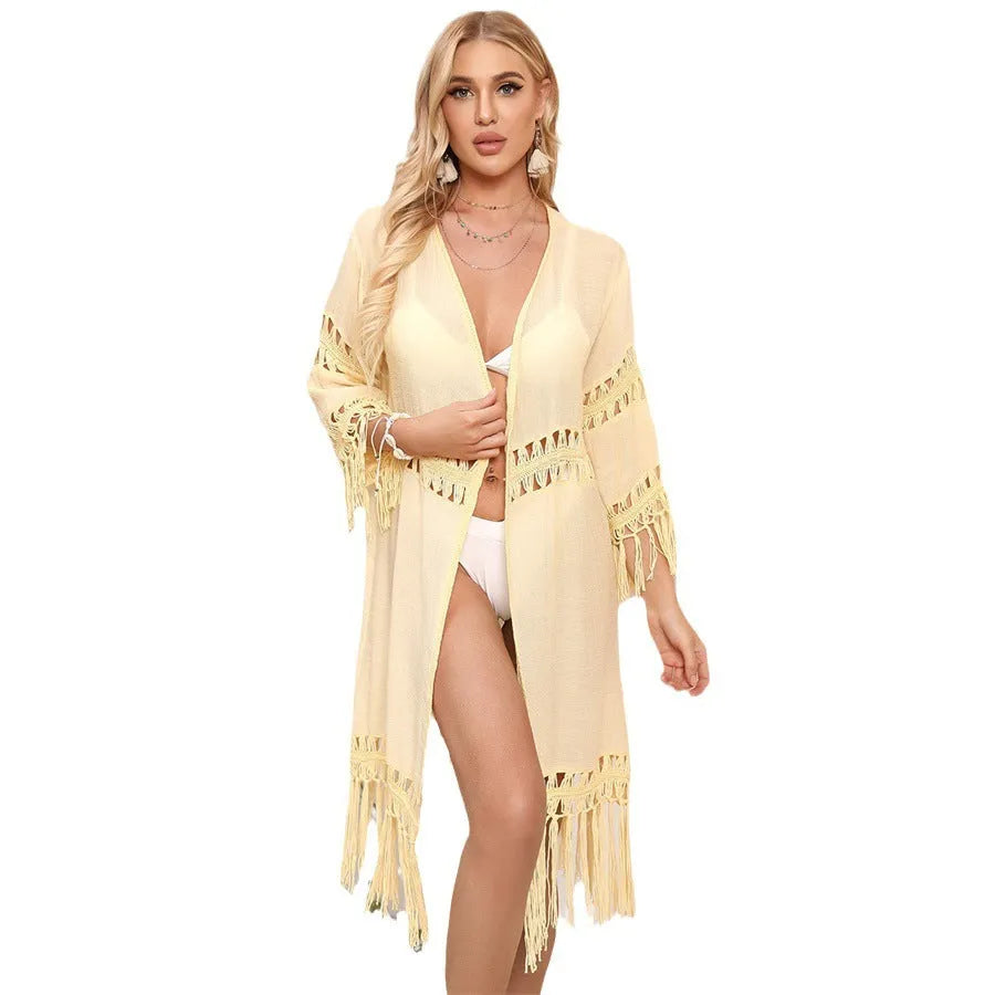Yellow acrylic crochet beach cardigan with tassel trim, shown on a hanger.
