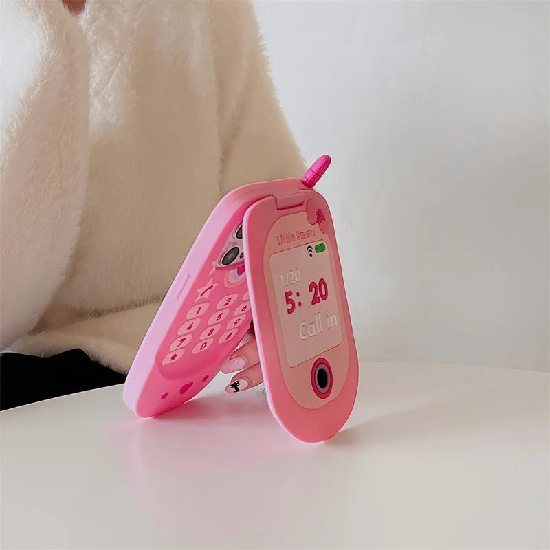 Light pink silicone flip phone case with a pop-out mirror and a cartoon charm, shown next to an iPhone.