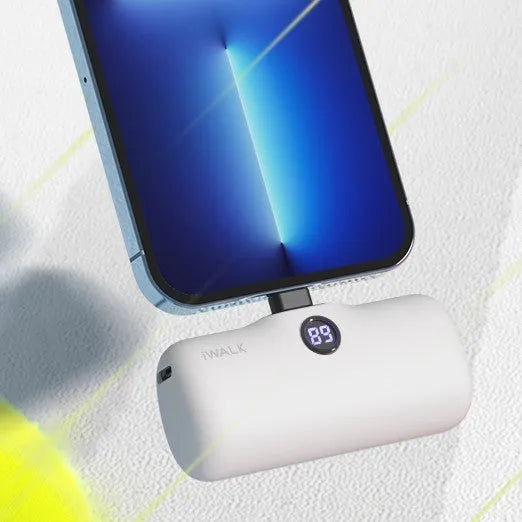Compact white lipstick-shaped power bank with digital battery percentage display on a wooden table.