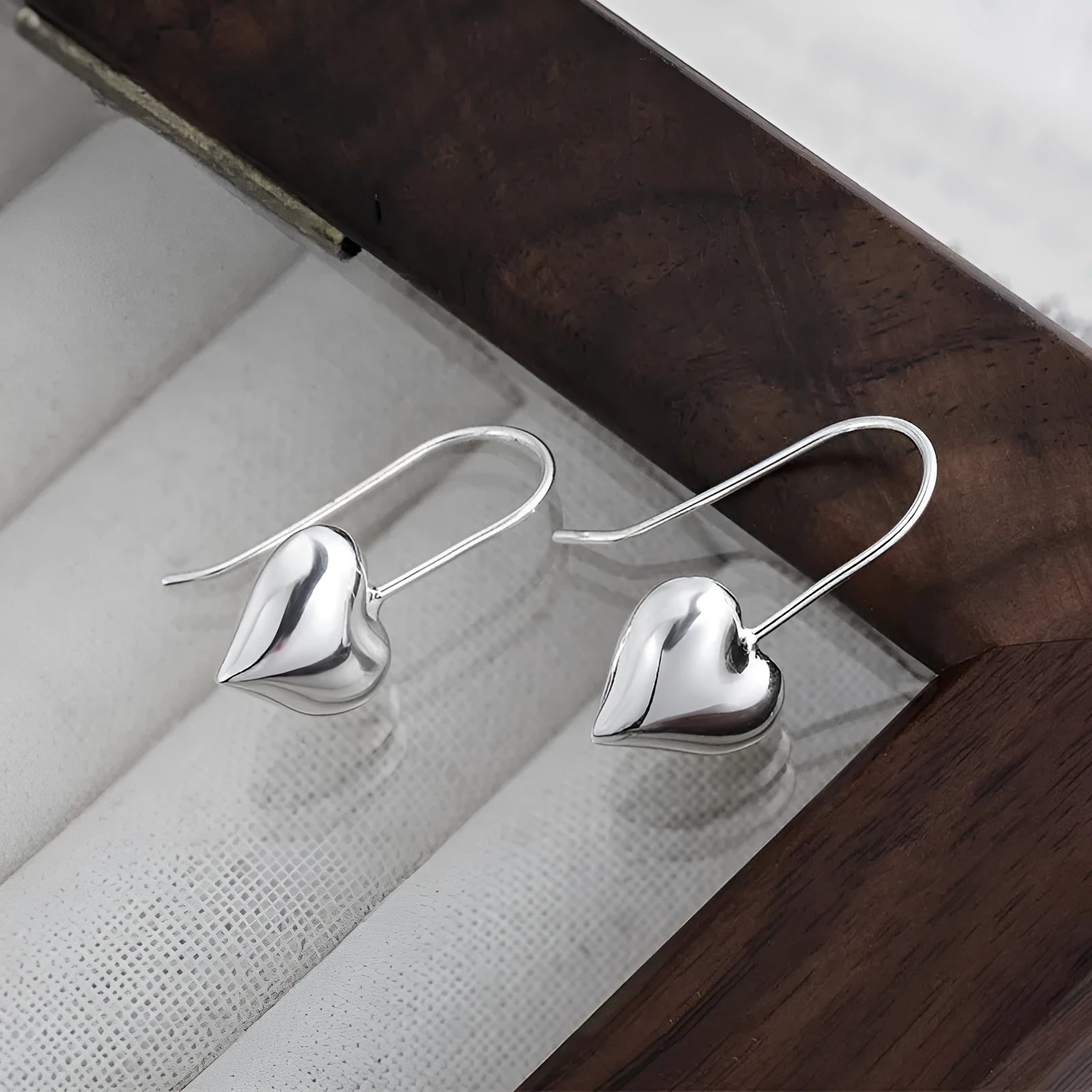 Silver coloured heart-shaped earrings with a glossy three-dimensional design on a white background.