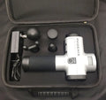 A black or silver ABS plastic percussion massage gun with four different removable massage heads on a table.