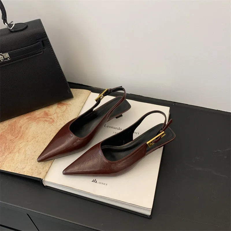 Women's black pointed toe leather shoes with a thin low heel and ankle strap on a rubber sole.