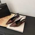 Women's black pointed toe leather shoes with a thin low heel and ankle strap on a rubber sole.