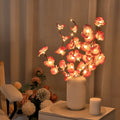 Pink fabric and plastic LED Phalaenopsis orchid branch light, 65cm long, on a table providing warm white ambient glow.