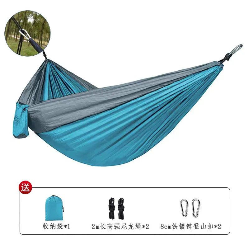 Blue parachute nylon camping hammock hung between two trees, showing its full 270cm length and attachment carabiners.