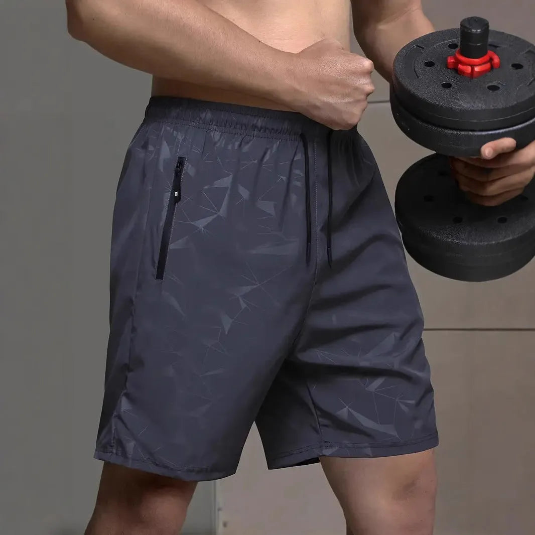 Man wearing loose-fit black printed sports shorts with an elasticated waist on a beach.