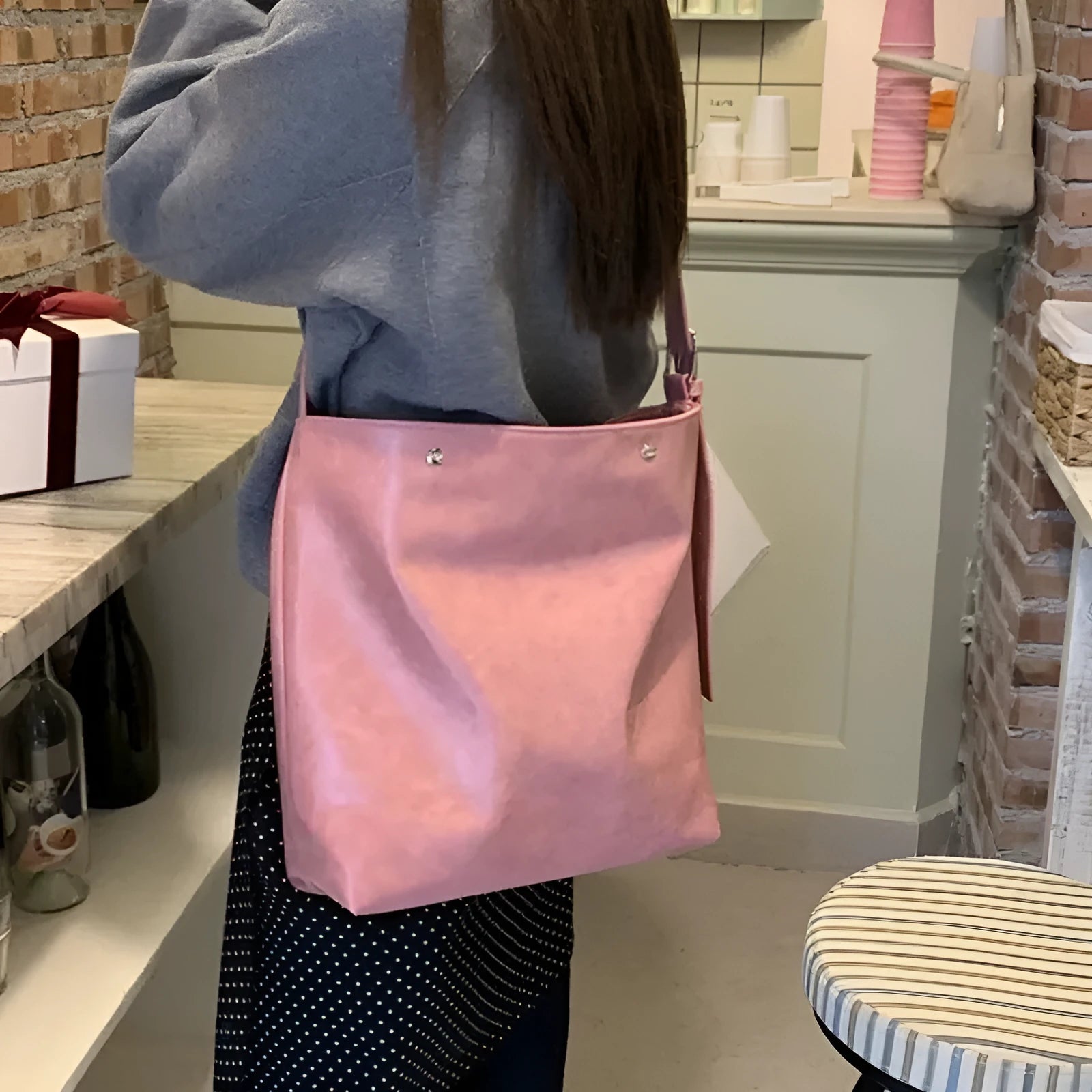Corduroy one-shoulder messenger bag in pink on a table, showing adjustable strap and structured shape.