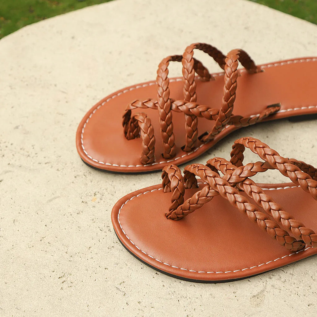 Women's flat woven sandals in black with a clip-toe design and rubber sole on a wooden surface.