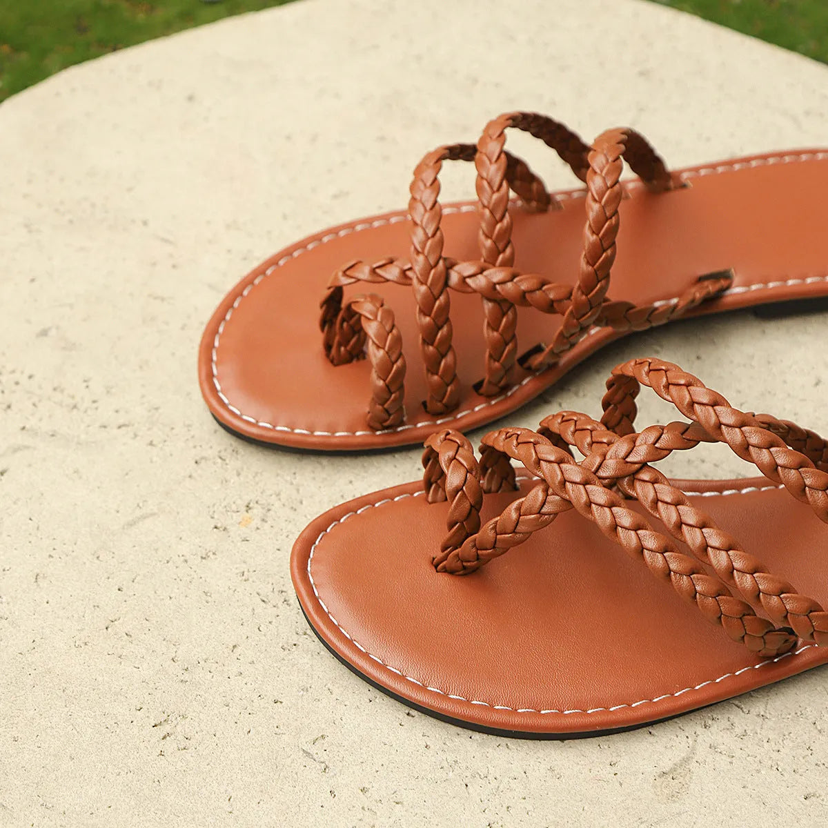 Women's flat woven sandals in black with a clip-toe design and rubber sole on a wooden surface.