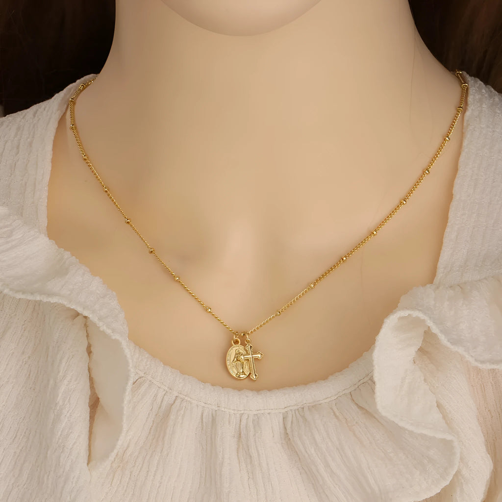 Geometric gold Virgin Mary and cross pendant necklace on a chain, showing minimalist design.