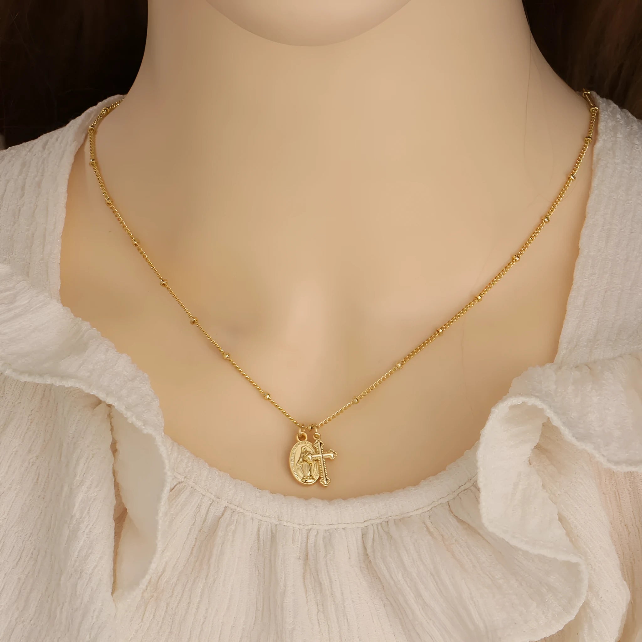 Geometric gold Virgin Mary and cross pendant necklace on a chain, showing minimalist design.