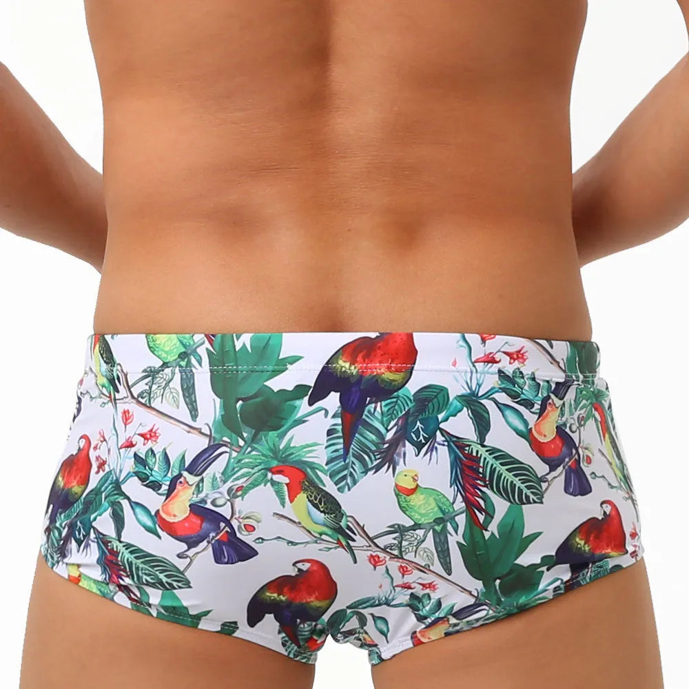 Men's blue swimming trunks with a detailed floral and bird print pattern, small boxer style