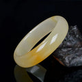 A polished light jade bracelet in a classic Chinese style band design on a plain background.
